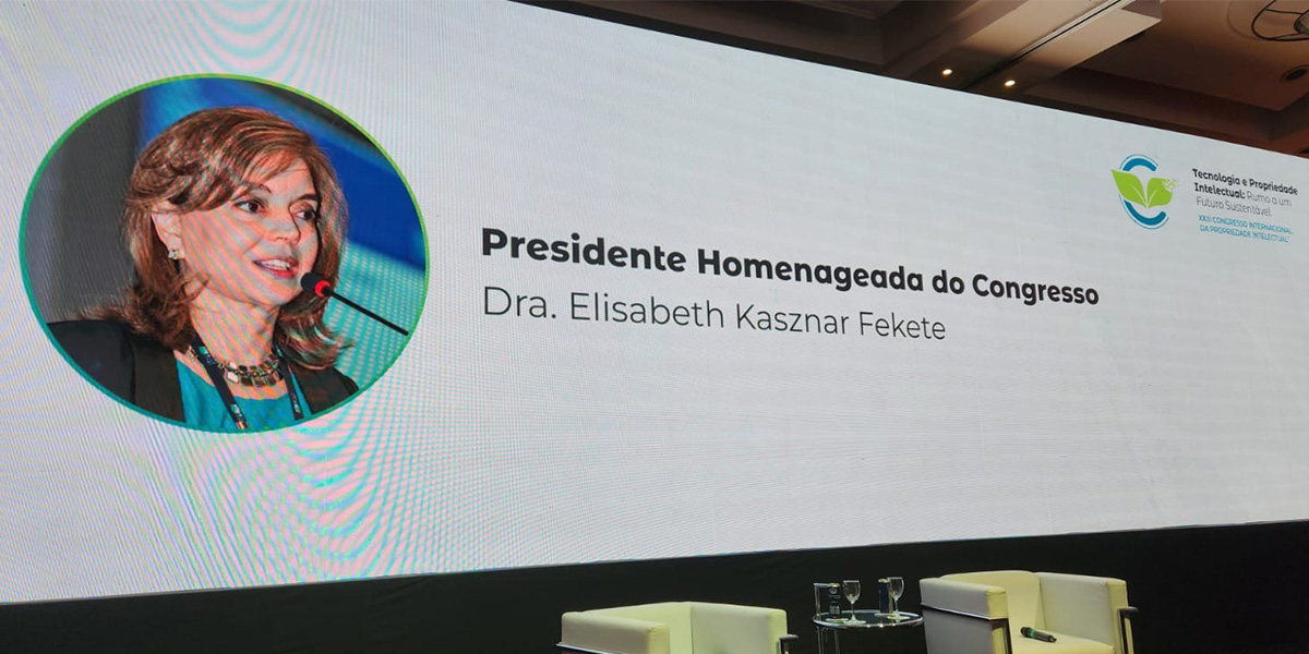Imagem de um telão com a nossa sócia Elisabeth Kasznar Fekete, indicando a sua nomeação, no XXIII Congresso Internacional da Propriedade Intelectual da Associação Paulista da Propriedade Intelectual, como Presidente Homenageada do Congresso,
